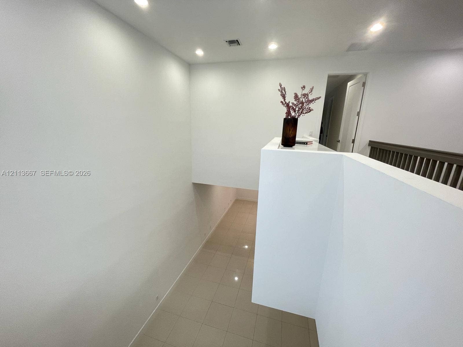 High-ceiling landing featuring tile flooring, recessed lighting, and a painted wooden guardrail