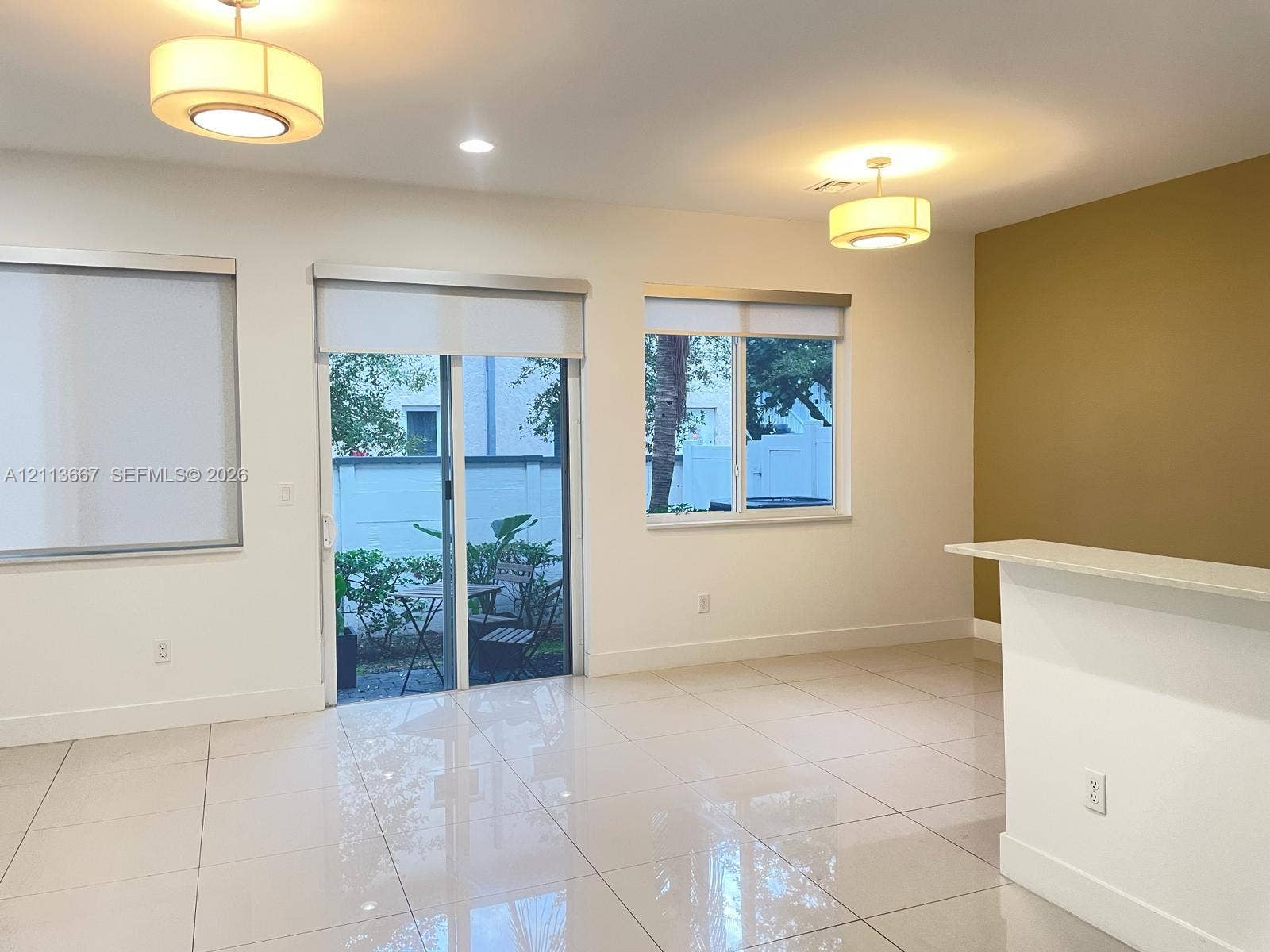 Interior space featuring large-format tile flooring, dual drum pendant lighting, a glass sliding door with integrated window shades, and a built-in counter
