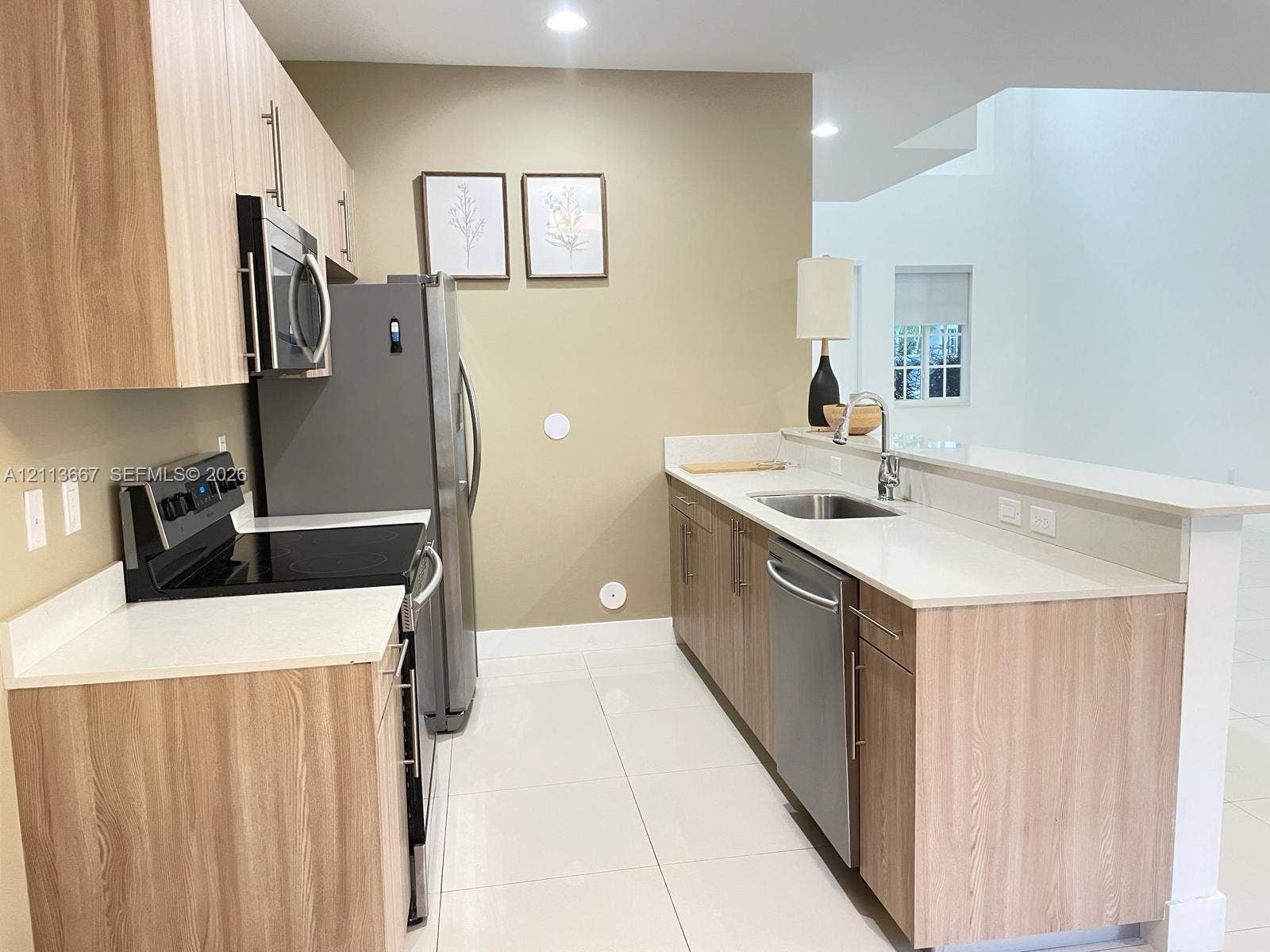 Kitchen featuring light wood-finish cabinetry, white countertops, stainless steel appliances, and tile flooring