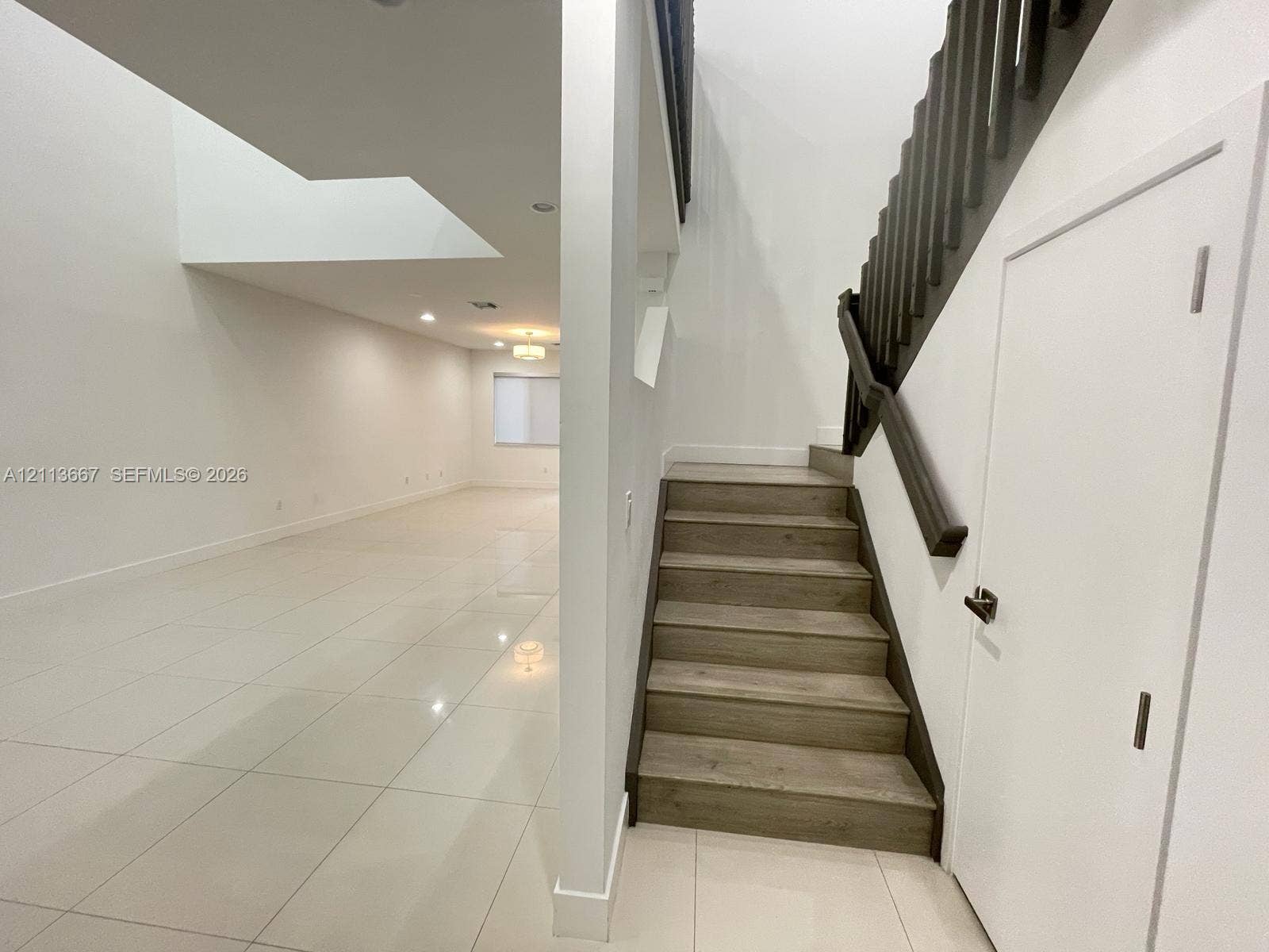 Staircase featuring wood-finish treads and a dark-toned railing, complemented by large-format tile flooring and recessed lighting