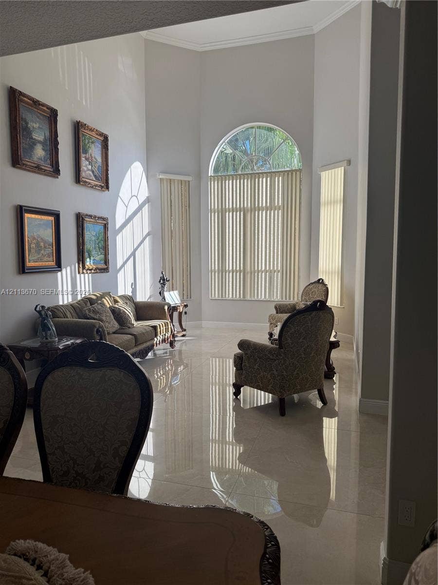 High-ceilinged living area featuring large-format polished tile flooring, an expansive arched window, and neutral wall tones
