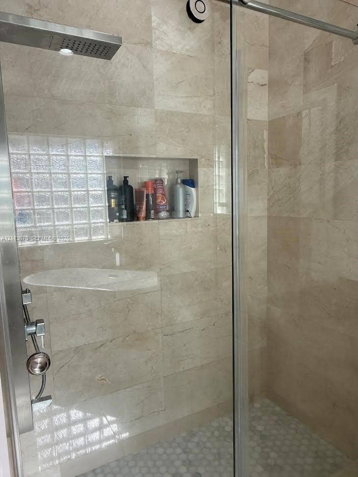 Walk-in shower featuring natural stone wall tile, built-in recessed wall niche, rainfall shower head, glass-block window, and pebble-style floor tile