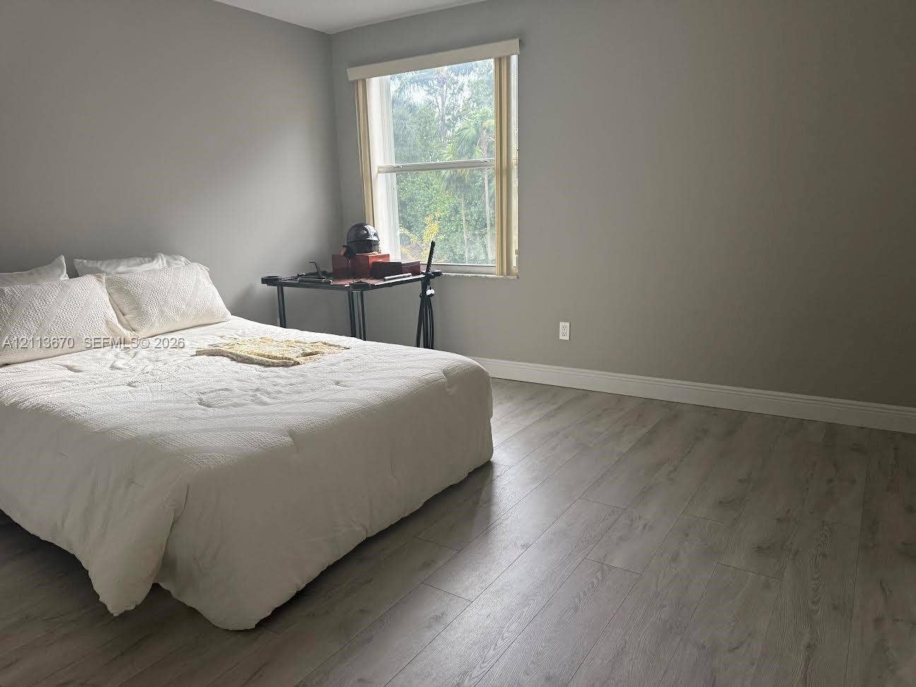 Room featuring wood-finish flooring, neutral wall tones, and a single-hung window with roller shade