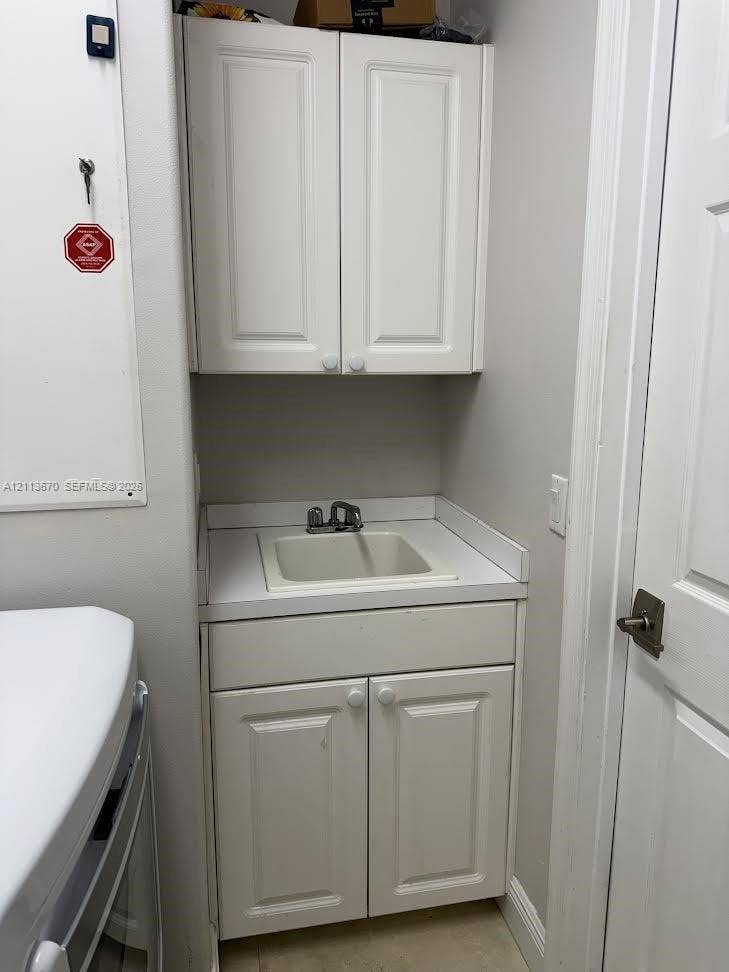 Built-in cabinetry featuring white shaker-style doors, integrated drop-in sink with dual-handle faucet, and solid-surface countertop