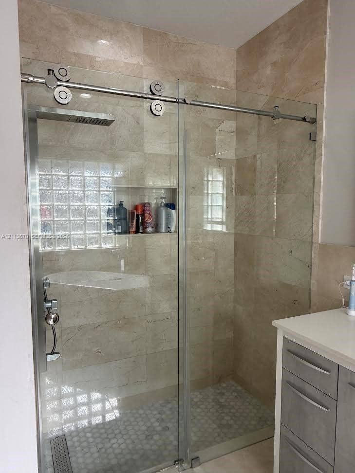 Walk-in shower featuring a sliding glass door with stainless steel hardware, floor-to-ceiling neutral tile, a built-in recessed wall niche, a rain-style showerhead, and a hexagon-tiled shower floor