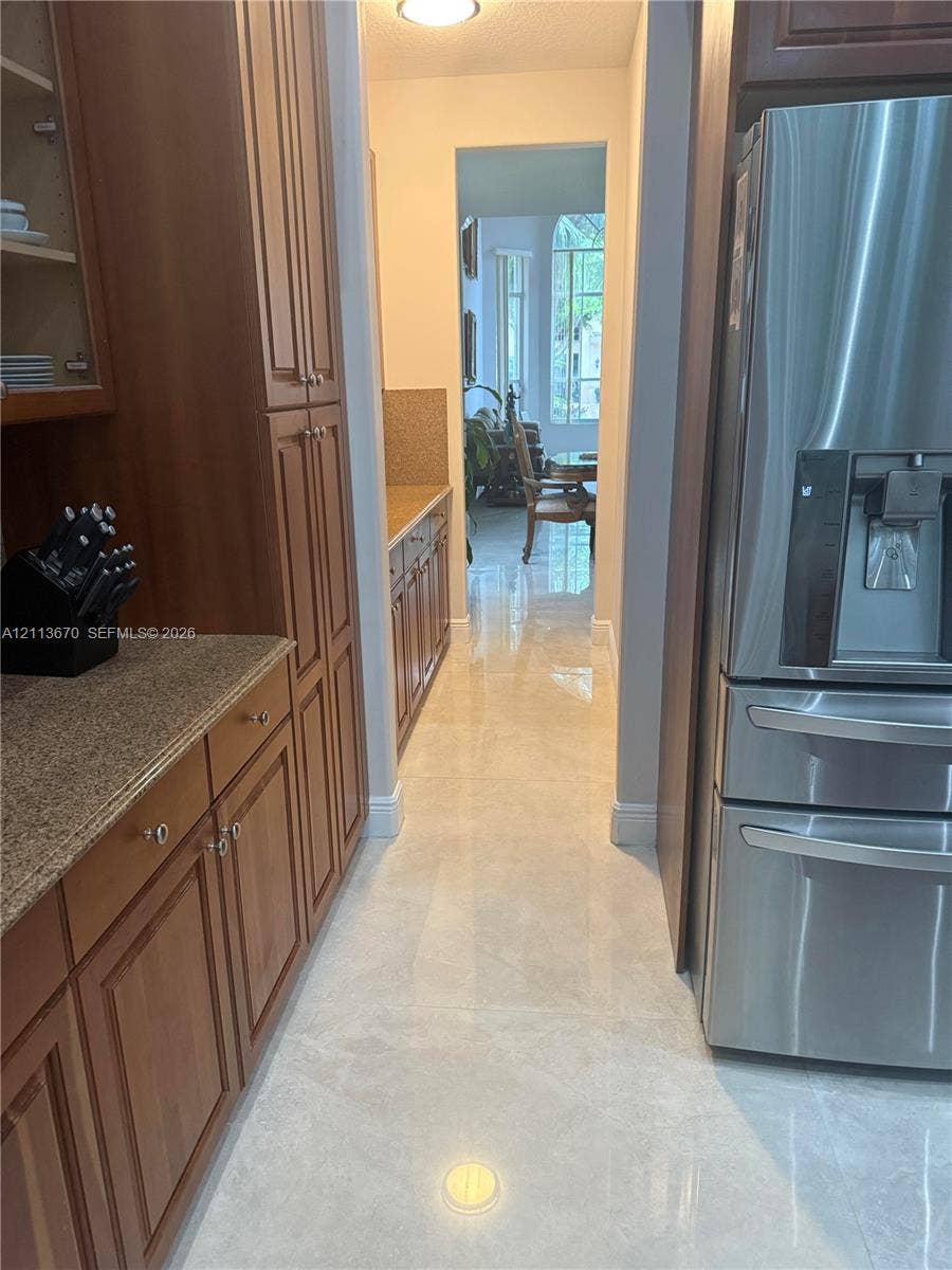 Kitchen featuring custom-built wood cabinetry, stone countertops, large-format tile flooring, and a stainless steel refrigerator