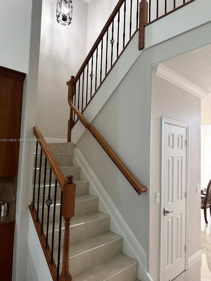 Staircase featuring stone-finish treads, wooden handrails, decorative wrought iron balusters, and a tiered metal chandelier