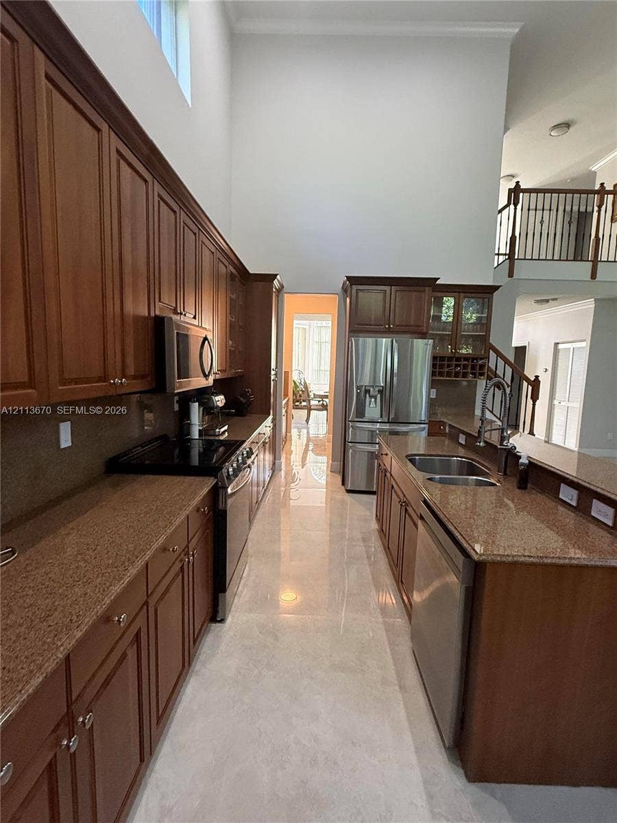 Kitchen featuring stained wood cabinetry, stone countertops, stainless steel appliances, double-basin sink, and high ceilings