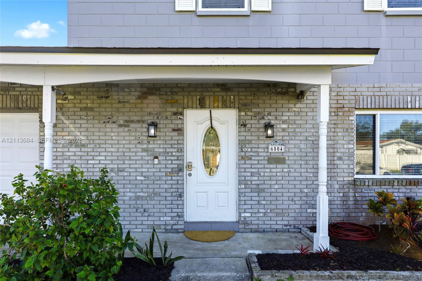 6504 Lenore Drive, Tampa, Tampa, FL 33634 Exterior facade featuring light-toned brick masonry, a covered porch with spindle columns, and an entry door with an oval glass insert
