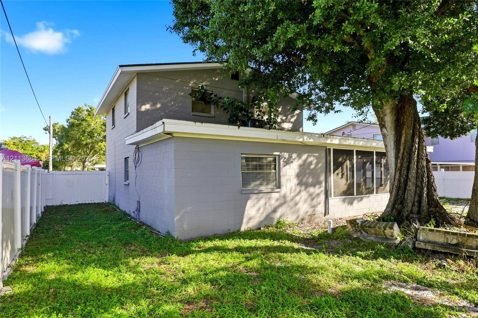 6504 Lenore Drive, Tampa, Tampa, FL 33634 Two-story exterior featuring painted concrete block construction, a screened-in rear enclosure, and white vinyl privacy fencing