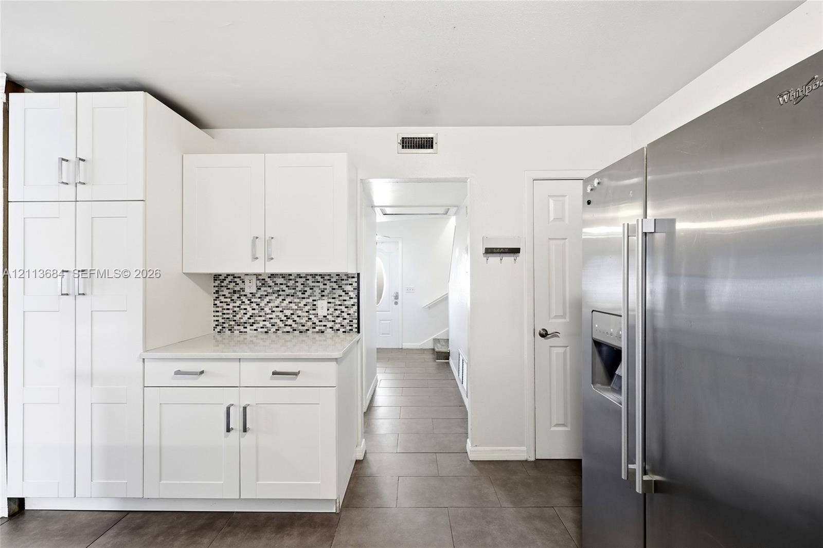 6504 Lenore Drive, Tampa, Tampa, FL 33634 White shaker-style cabinetry with rectangular hardware, stone-composite countertop, geometric tile backsplash, large-format tile flooring, and stainless steel side-by-side refrigerator