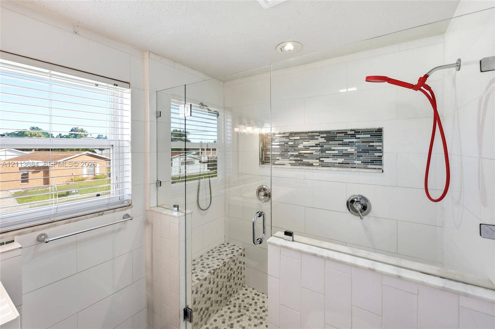 6504 Lenore Drive, Tampa, Tampa, FL 33634 Walk-in shower featuring a glass enclosure, built-in tiled bench, mosaic stone flooring, recessed decorative tile inlay, and polished chrome fixtures