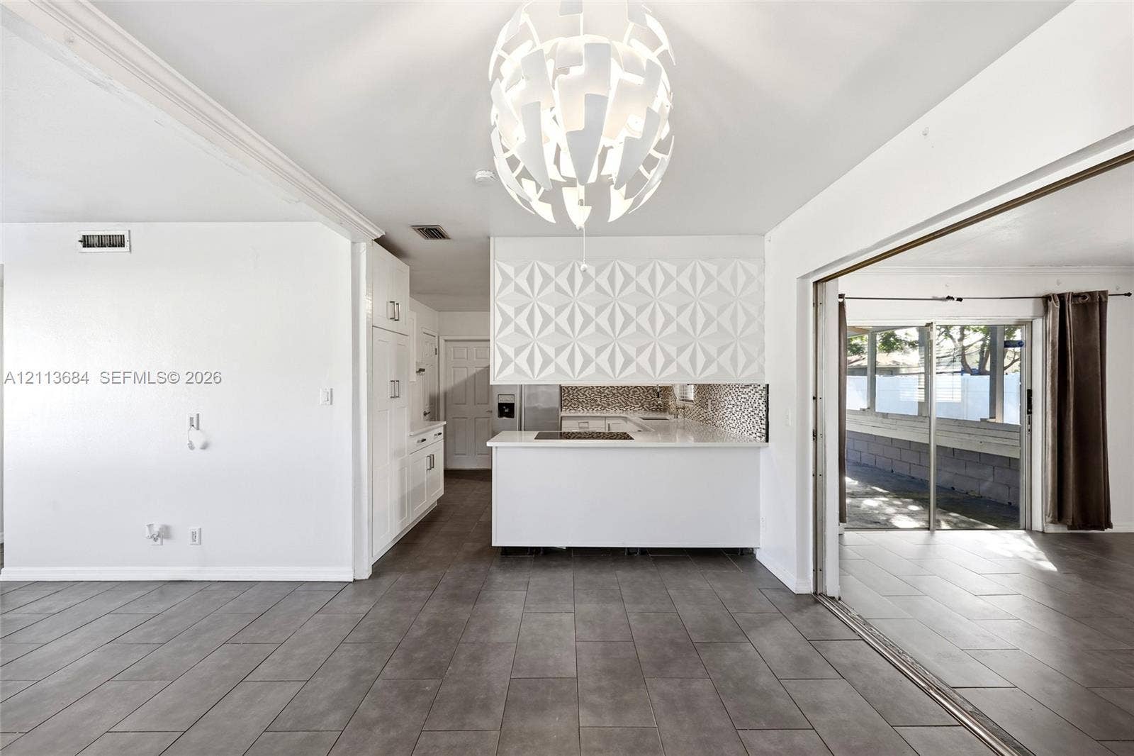 6504 Lenore Drive, Tampa, Tampa, FL 33634 Interior featuring large-format tile flooring, a geometric-patterned backsplash, a white kitchen island, and a modern tiered pendant light fixture