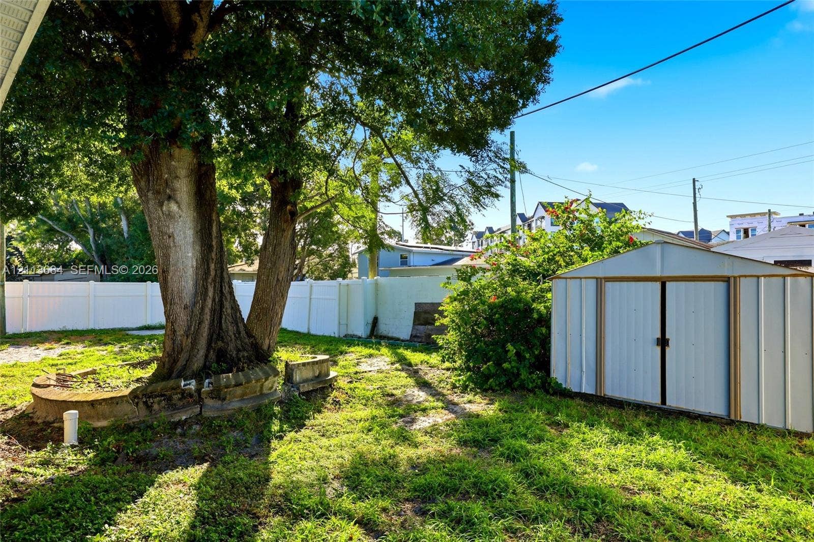 6504 Lenore Drive, Tampa, Tampa, FL 33634 Backyard featuring a white vinyl privacy fence, mature shade tree with a stone-accented perimeter, and a detached metal storage structure