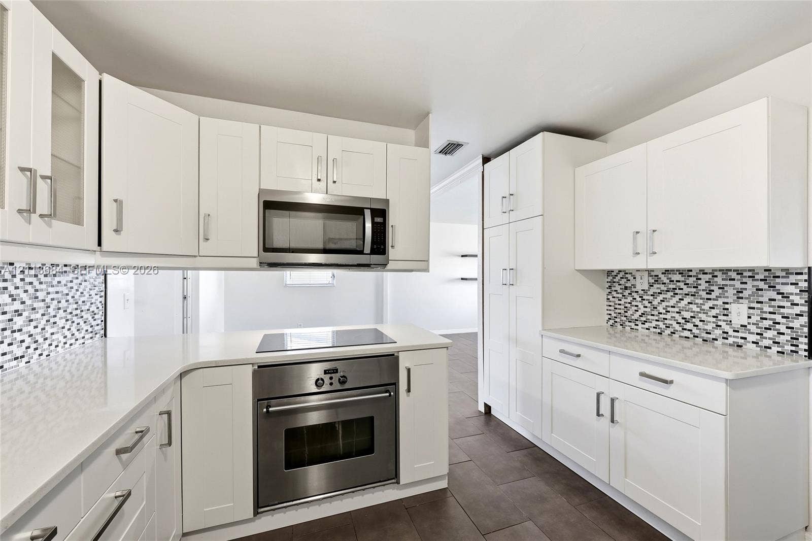 6504 Lenore Drive, Tampa, Tampa, FL 33634 Kitchen featuring white shaker-style cabinetry, solid-surface countertops, a geometric mosaic tile backsplash, stainless steel built-in oven and microwave, and large-format tile flooring