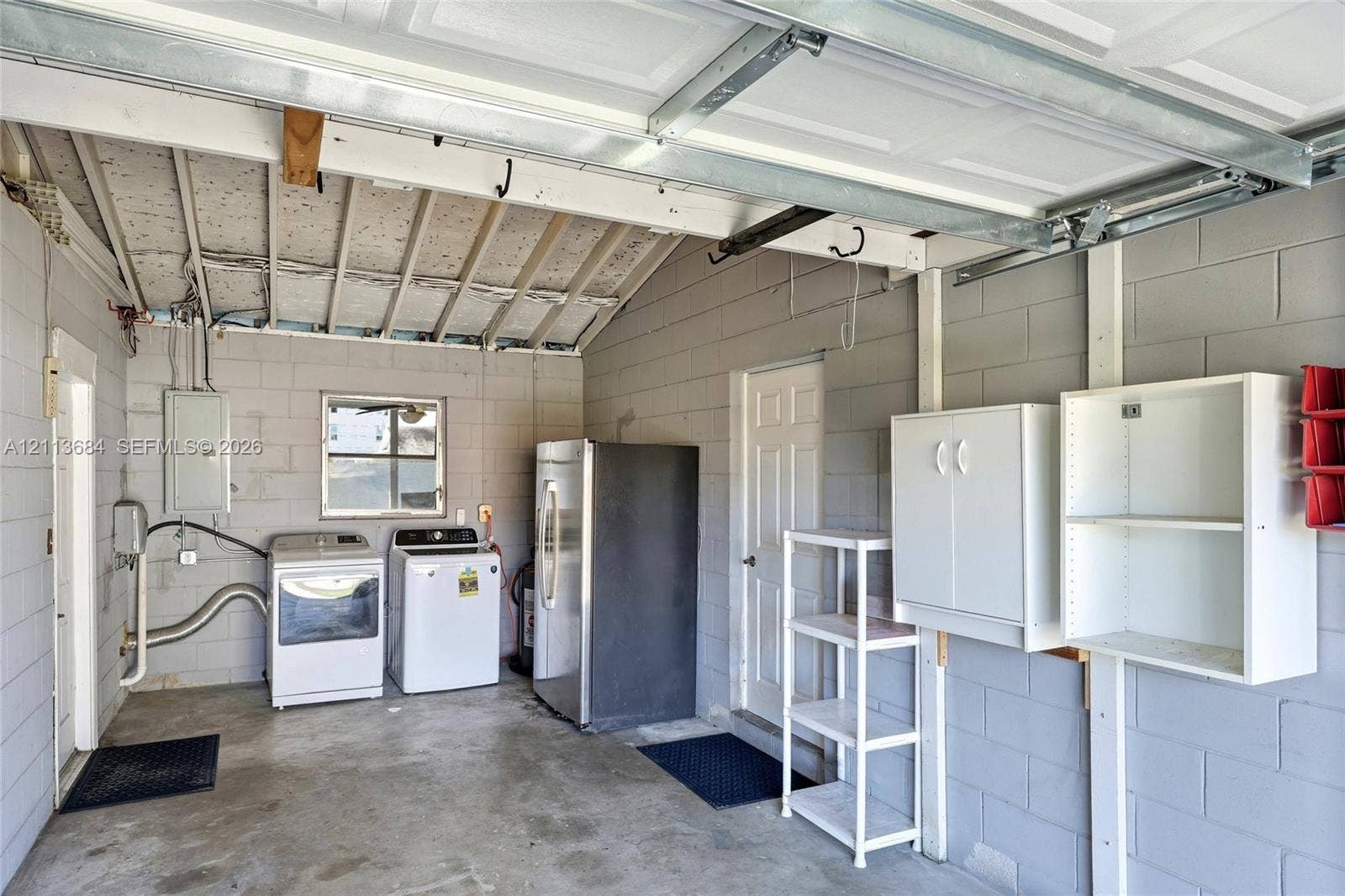 6504 Lenore Drive, Tampa, Tampa, FL 33634 Garage featuring concrete block walls, exposed rafter ceiling, multiple wall-mounted storage cabinets, and dedicated utility hookups