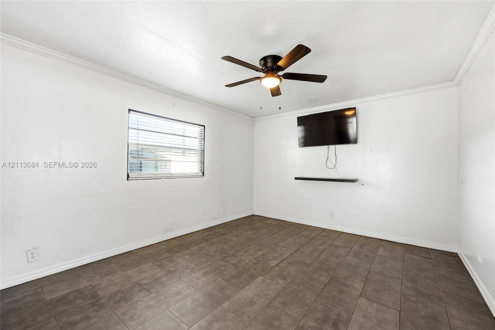 6504 Lenore Drive, Tampa, Tampa, FL 33634 Neutral-toned room featuring large-format tile flooring, a dark-finish ceiling fan with integrated lighting, and a horizontal wall-mounted display shelf