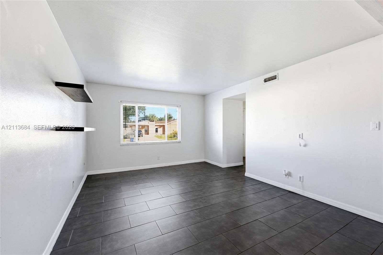 6504 Lenore Drive, Tampa, Tampa, FL 33634 Interior space featuring large-format dark grey tile flooring, neutral wall finishes, a single-pane window, and two wall-mounted floating shelves