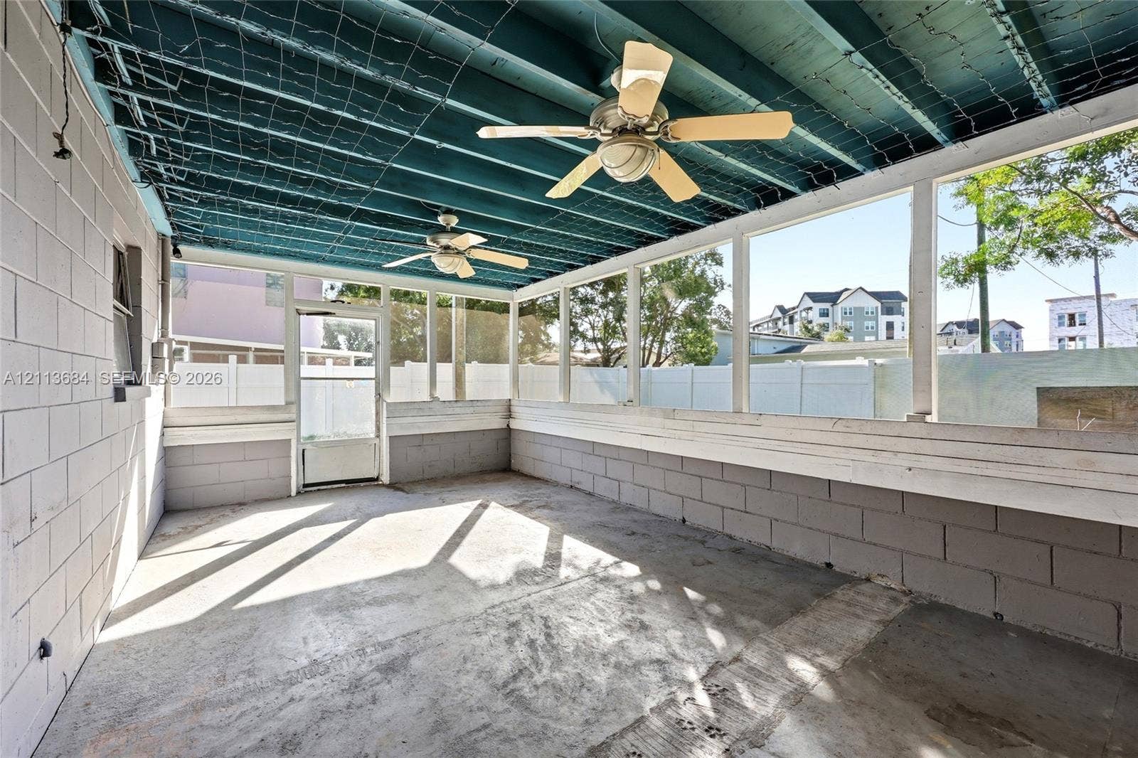 6504 Lenore Drive, Tampa, Tampa, FL 33634 Screened-in porch featuring painted concrete block walls, a concrete floor, two ceiling fans, and an exposed ceiling structure