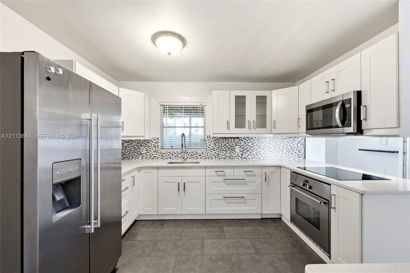6504 Lenore Drive, Tampa, Tampa, FL 33634 Kitchen featuring white cabinetry, stainless steel appliances, patterned tile backsplash, light-colored countertops, and tile flooring
