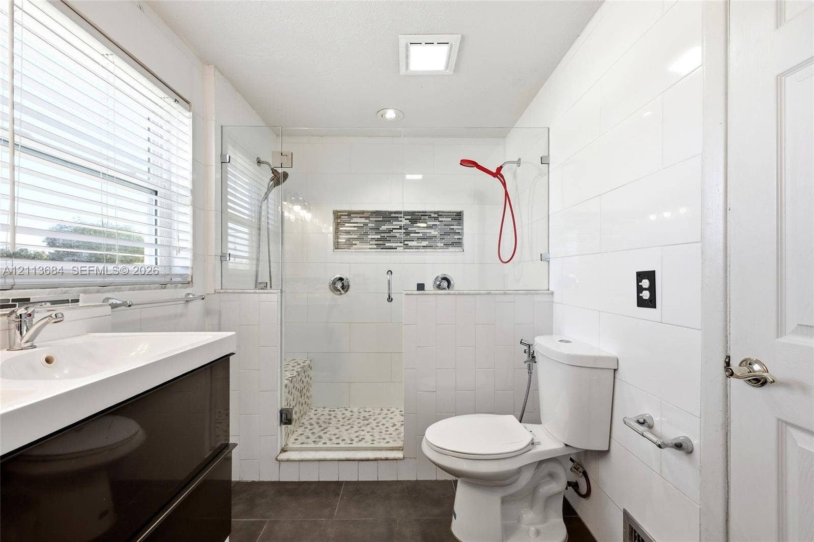 6504 Lenore Drive, Tampa, Tampa, FL 33634 Walk-in shower with frameless glass enclosure, pebble-stone flooring, horizontal mosaic tile inlay, and wall-mounted plumbing fixtures, paired with a modern dark-finish vanity