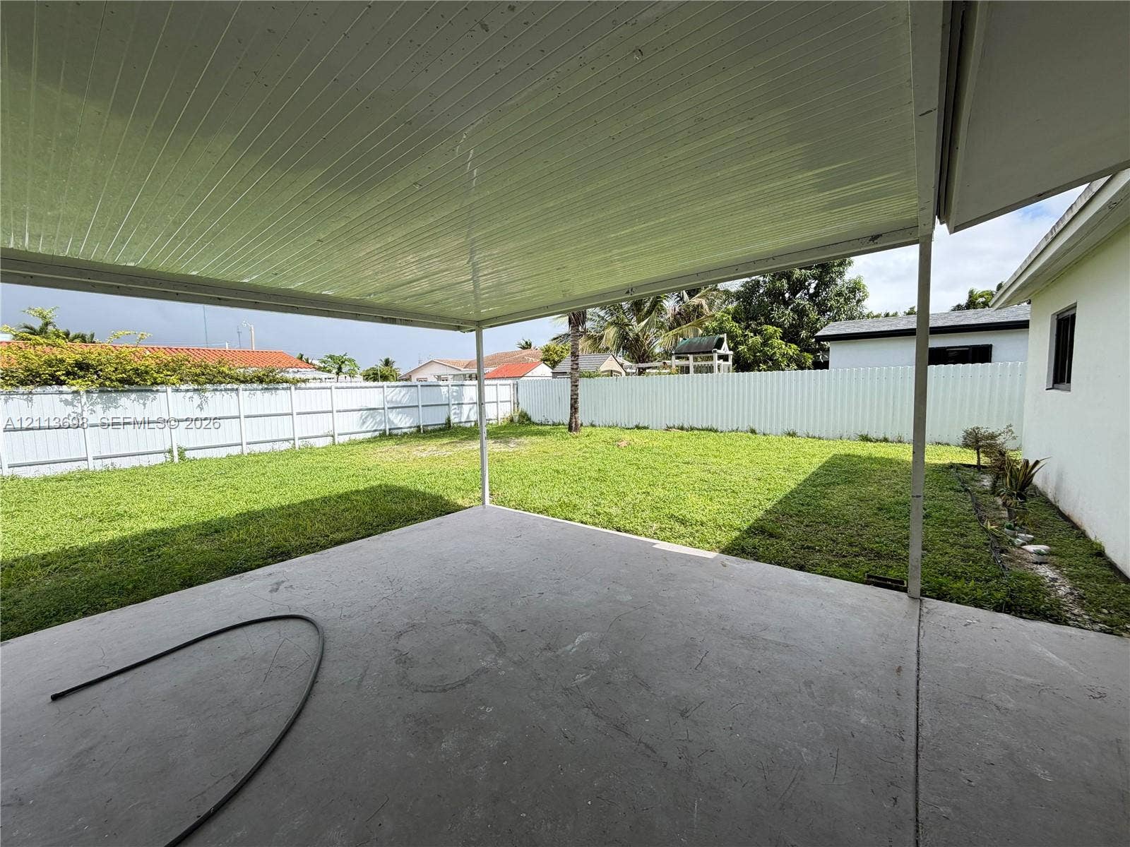 115 NE 205th Terrace, Miami Gardens, FL 33179 Covered concrete patio with a solid roof structure, expansive fenced backyard, and level lawn