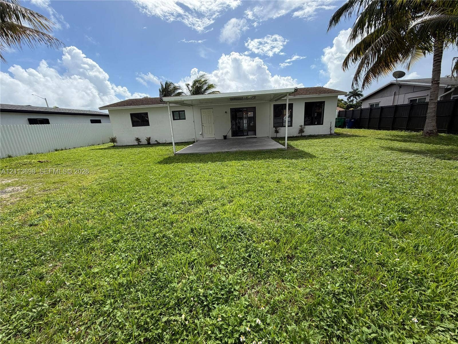 115 NE 205th Terrace, Miami Gardens, FL 33179 Expansive backyard featuring a covered concrete patio, solid perimeter fencing, and mature palm trees