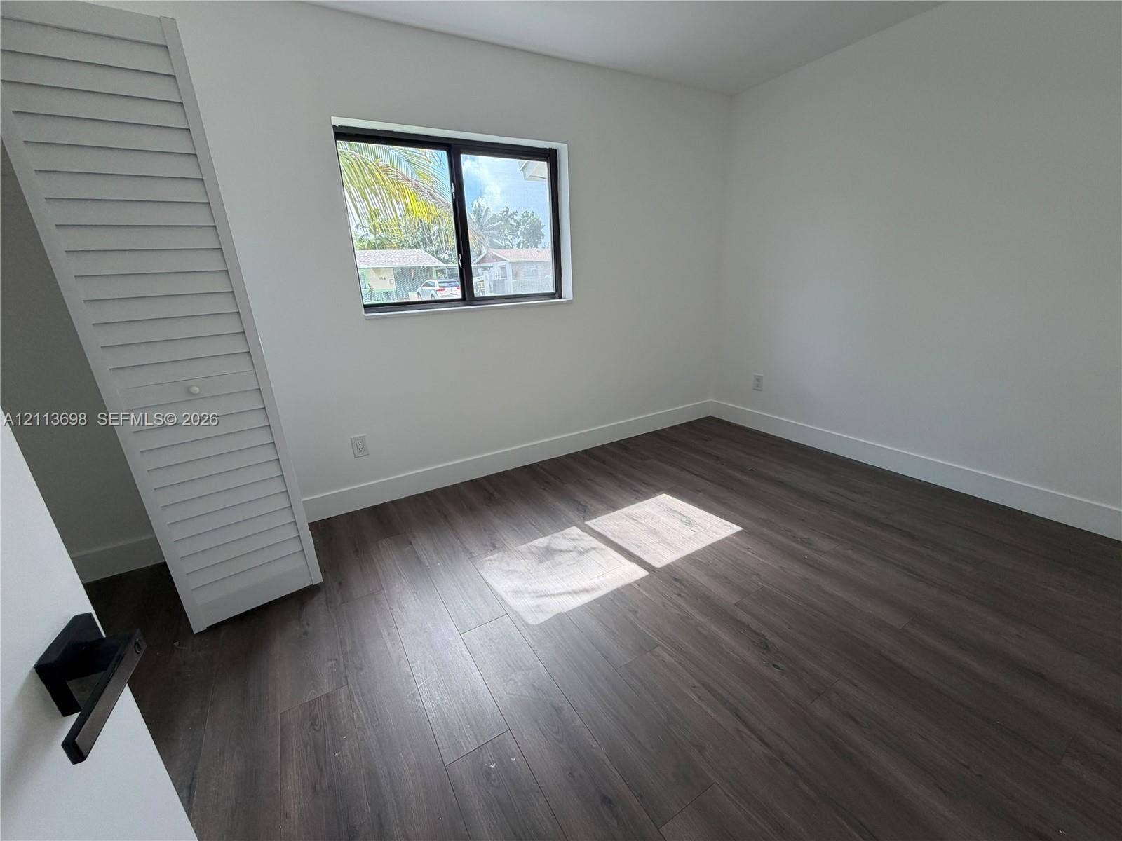 115 NE 205th Terrace, Miami Gardens, FL 33179 Room featuring wood-finish flooring, a single-panel window with a dark frame, and a louvered-door closet