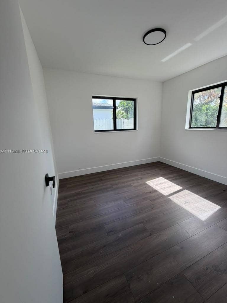 115 NE 205th Terrace, Miami Gardens, FL 33179 Interior room featuring wood-finish flooring, two windows with black frames, and a flush-mount ceiling light