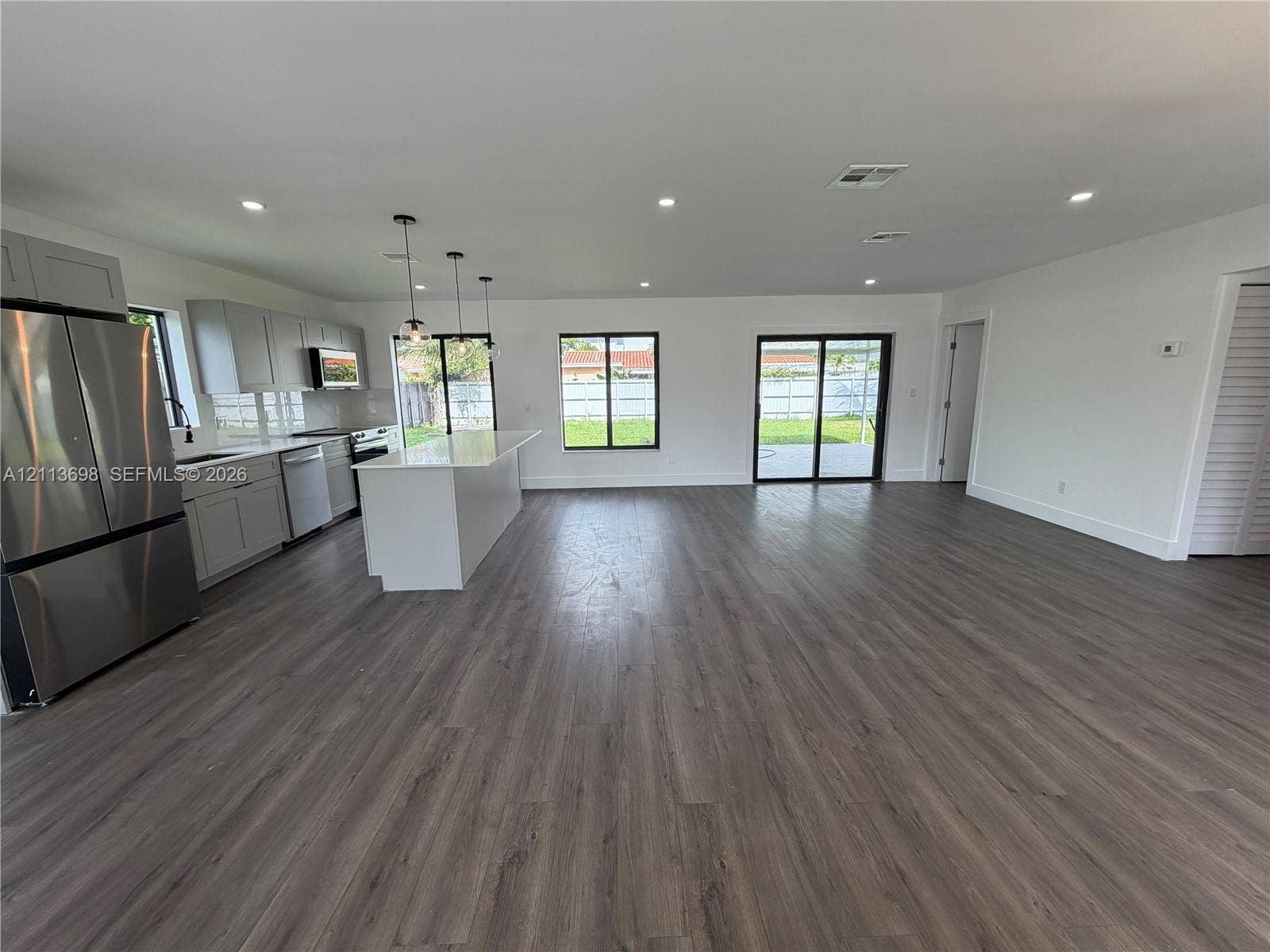 115 NE 205th Terrace, Miami Gardens, FL 33179 Open-concept kitchen featuring light grey cabinetry, a central island with a solid-surface countertop, stainless steel appliances, recessed lighting, and wood-finish flooring