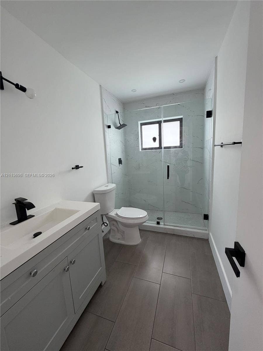 115 NE 205th Terrace, Miami Gardens, FL 33179 Bathroom featuring a gray vanity with an integrated basin, matte black fixtures, tile flooring, and a walk-in shower with a glass enclosure and wall-to-wall tiling