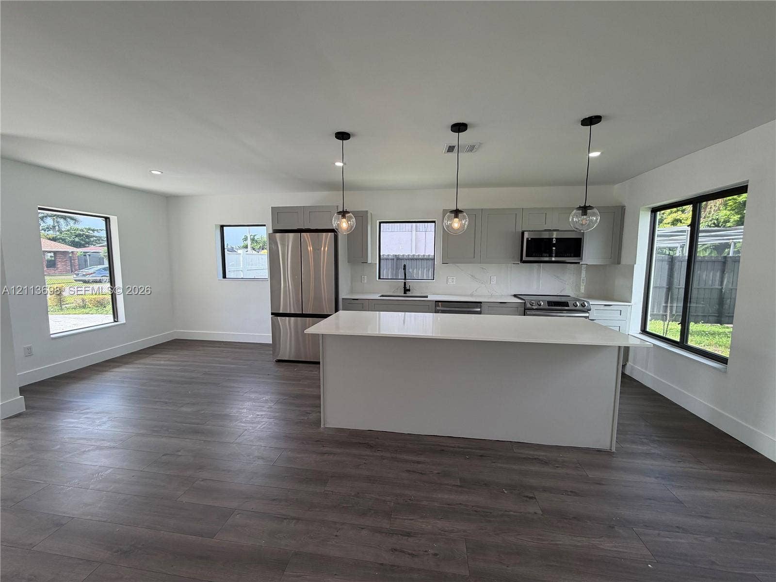 115 NE 205th Terrace, Miami Gardens, FL 33179 Kitchen featuring wood-finish flooring, quartz-surfaced island, shaker-style cabinetry, stainless steel appliances, and glass pendant lighting