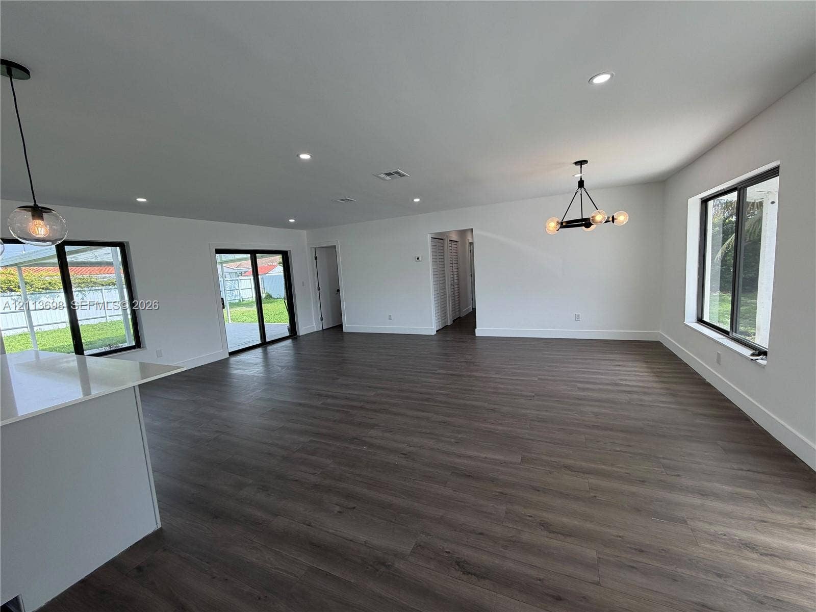 115 NE 205th Terrace, Miami Gardens, FL 33179 Open-concept interior featuring wood-finish flooring, recessed lighting, multi-arm chandelier, and sliding glass doors with dark frames
