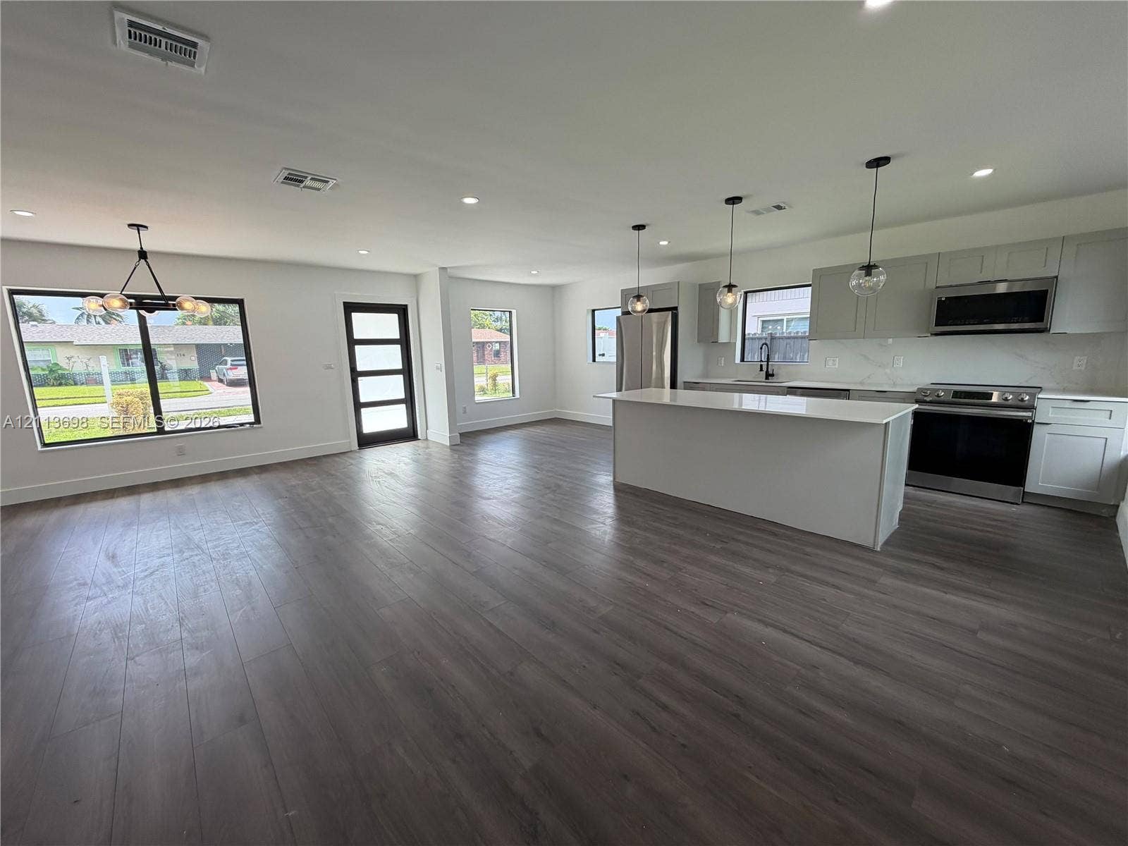 115 NE 205th Terrace, Miami Gardens, FL 33179 Open floor plan featuring wood-finish flooring, a kitchen island with stone-surface countertop, flat-panel cabinetry, stainless steel appliances, and multi-pendant lighting