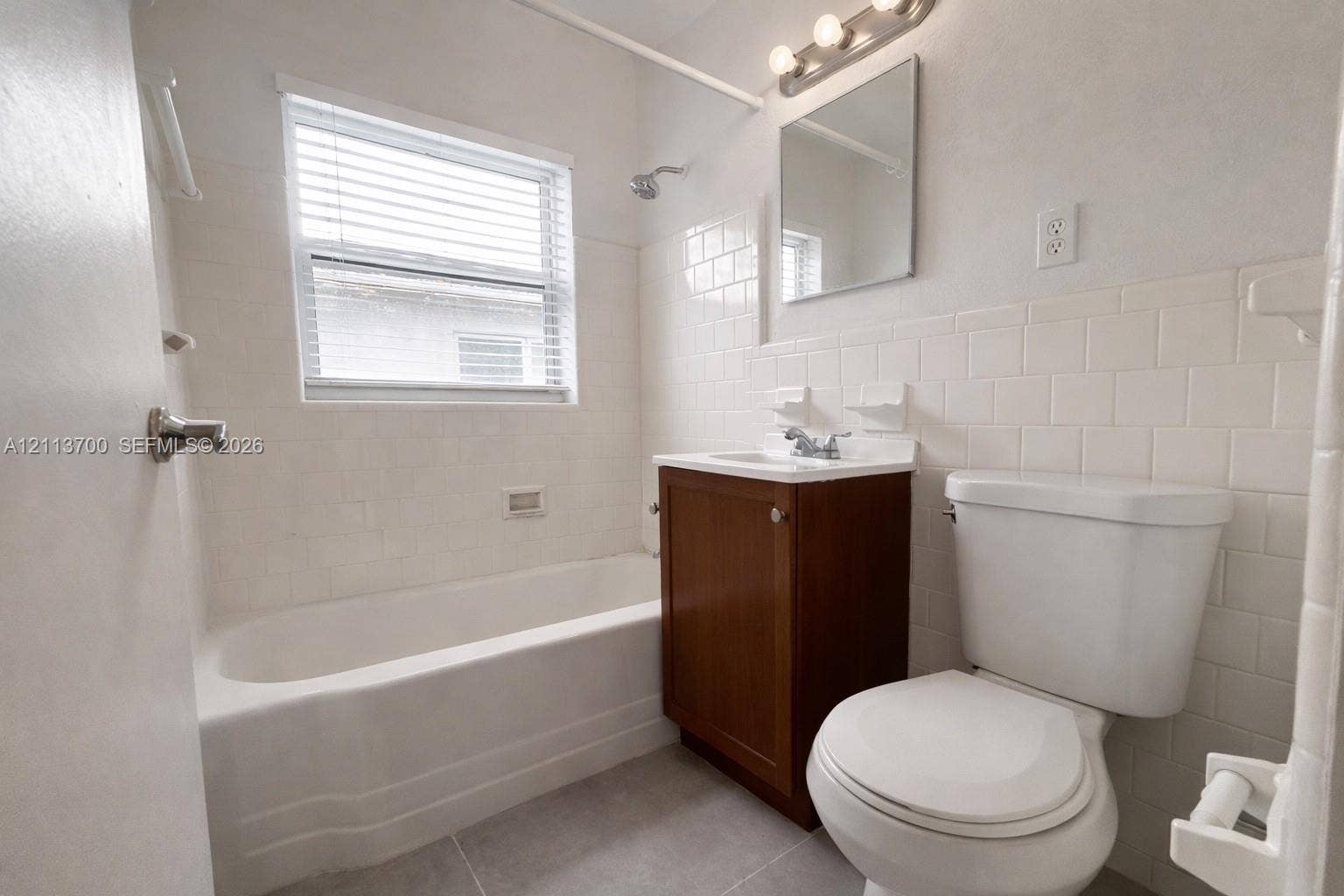 2707 Lincoln Street, #17-18, Hollywood, Hollywood, FL 33020 Bathroom featuring a single-sink vanity with a wood-finish cabinet, white subway tile shower surround, standard bathtub, and wall-mounted vanity lighting