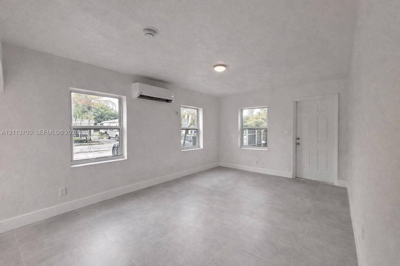 2707 Lincoln Street, #17-18, Hollywood, Hollywood, FL 33020 Neutral-toned tile flooring, three large windows, wall-mounted ductless climate control unit, and six-panel interior door