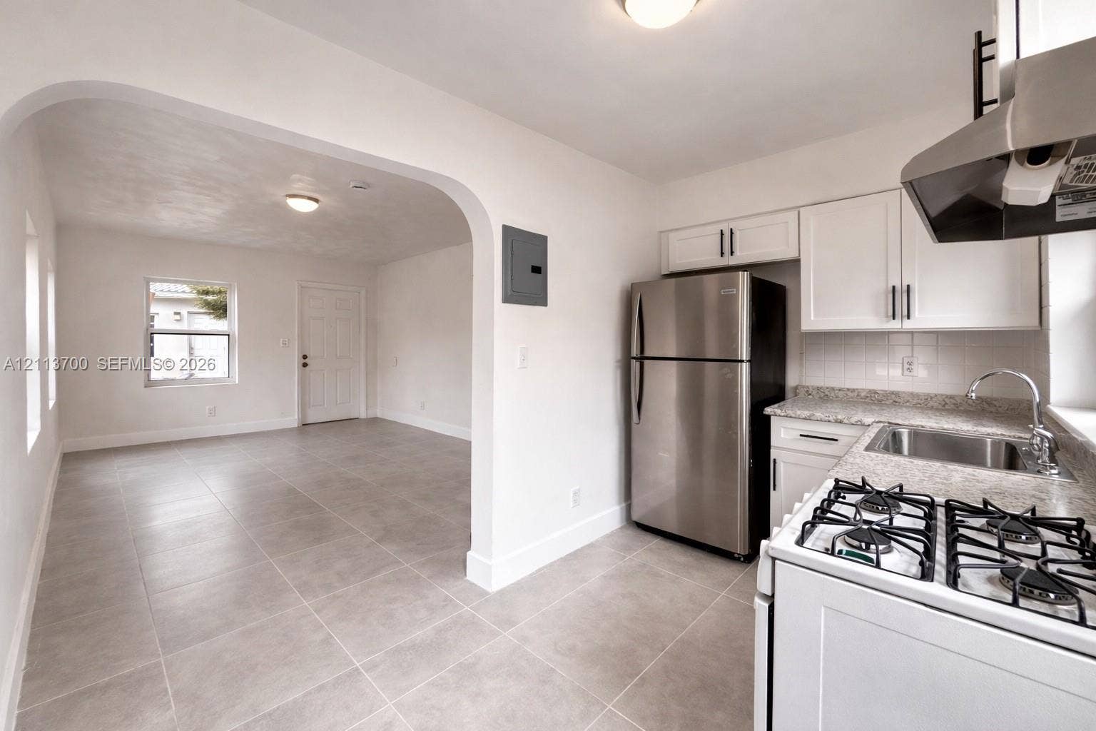 2707 Lincoln Street, #17-18, Hollywood, Hollywood, FL 33020 Kitchen featuring white Shaker-style cabinetry, stone-finish countertops, stainless steel appliances, and tile flooring, highlighted by an architectural arched wall opening
