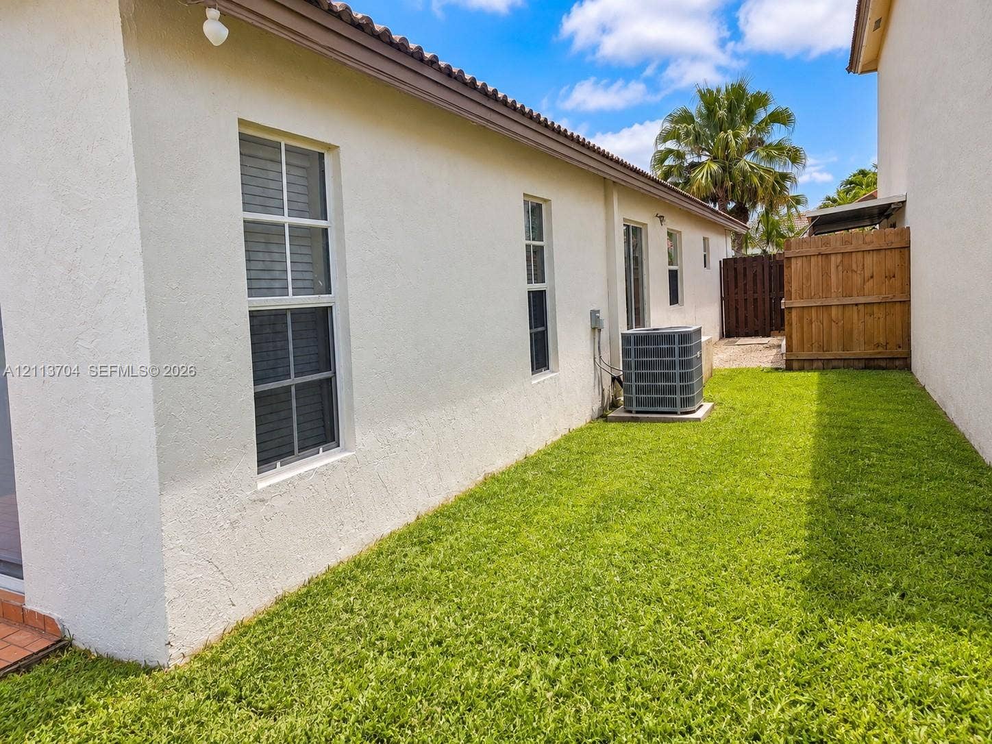 5254 SW 153rd Court, Miami, FL 33185 Stucco exterior with multi-pane windows and a side yard featuring a manicured lawn, wood privacy fencing, and exterior HVAC unit
