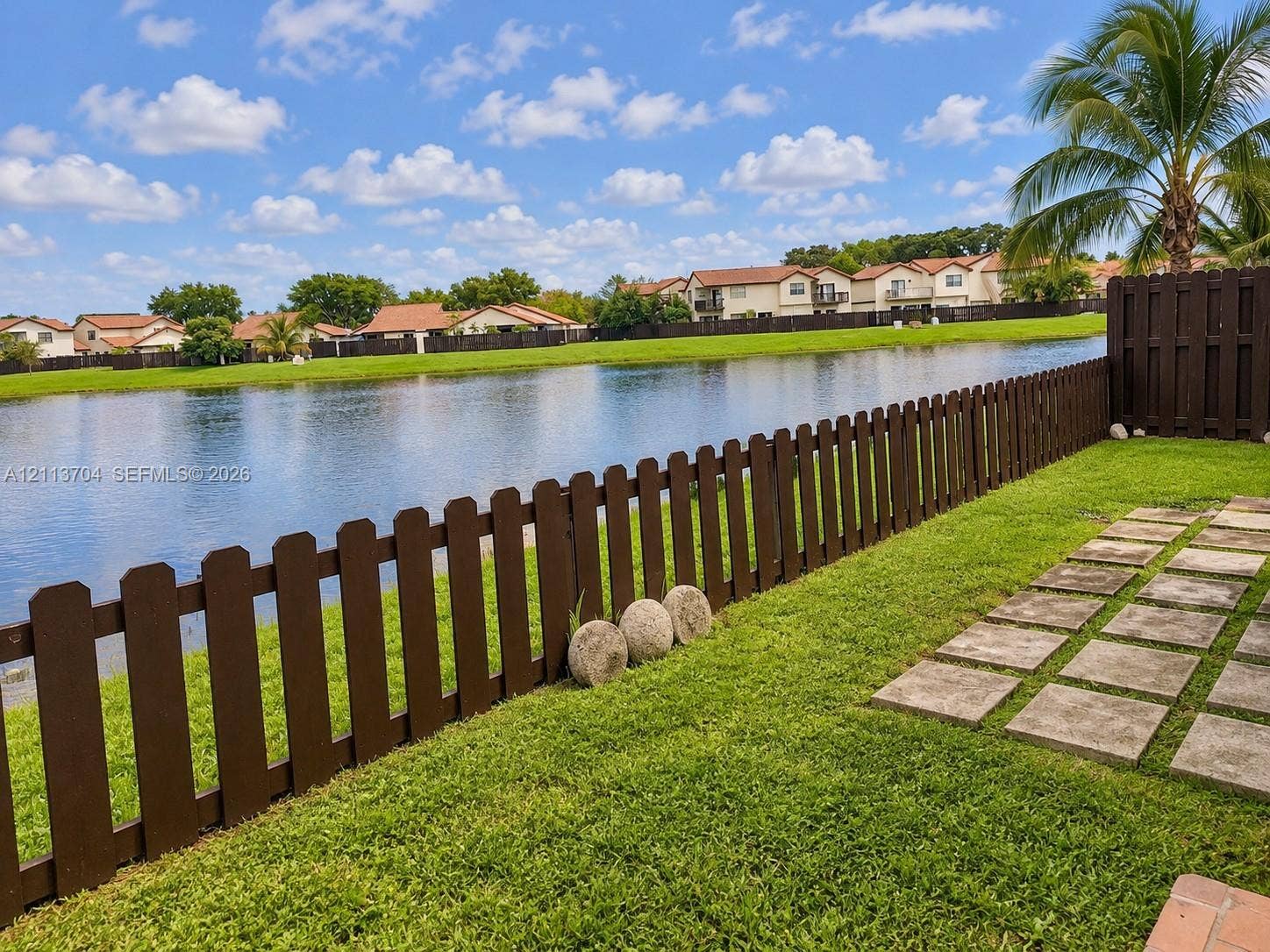 5254 SW 153rd Court, Miami, FL 33185 Waterfront backyard featuring a grass lawn, paved stone path, and dark wood-tone perimeter fencing