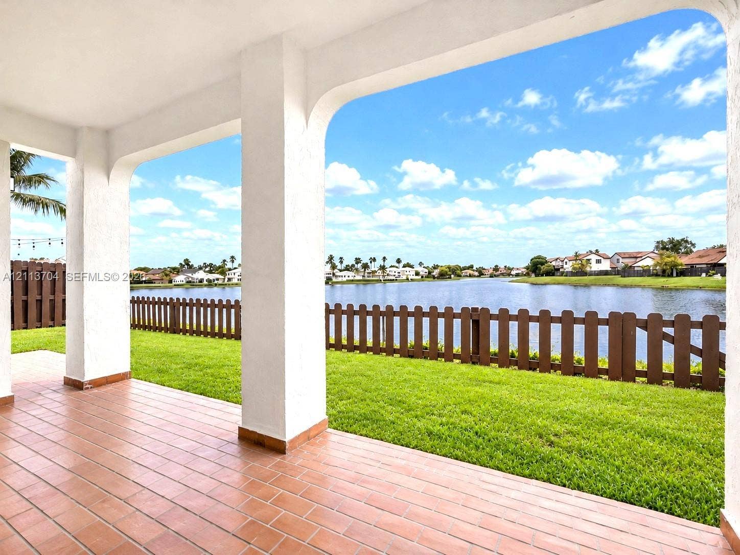 5254 SW 153rd Court, Miami, FL 33185 Covered patio featuring ceramic tile flooring, arched structural pillars, and direct water frontage with a wooden perimeter fence