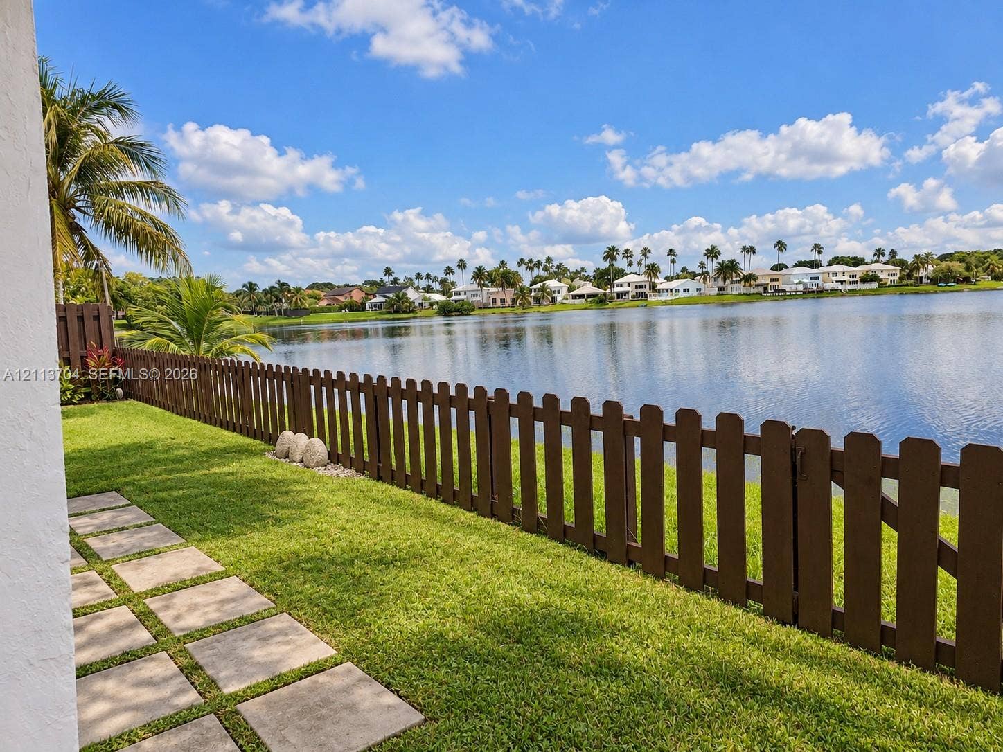5254 SW 153rd Court, Miami, FL 33185 Waterfront lot featuring a grass lawn, paved stone path, and dark brown wood-finish picket fencing