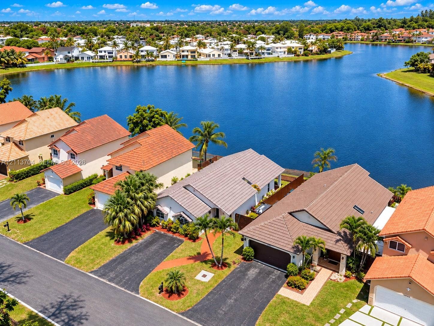 5254 SW 153rd Court, Miami, FL 33185 Waterfront residential property featuring tile roofing, asphalt driveways, mature palm trees, and manicured landscaping