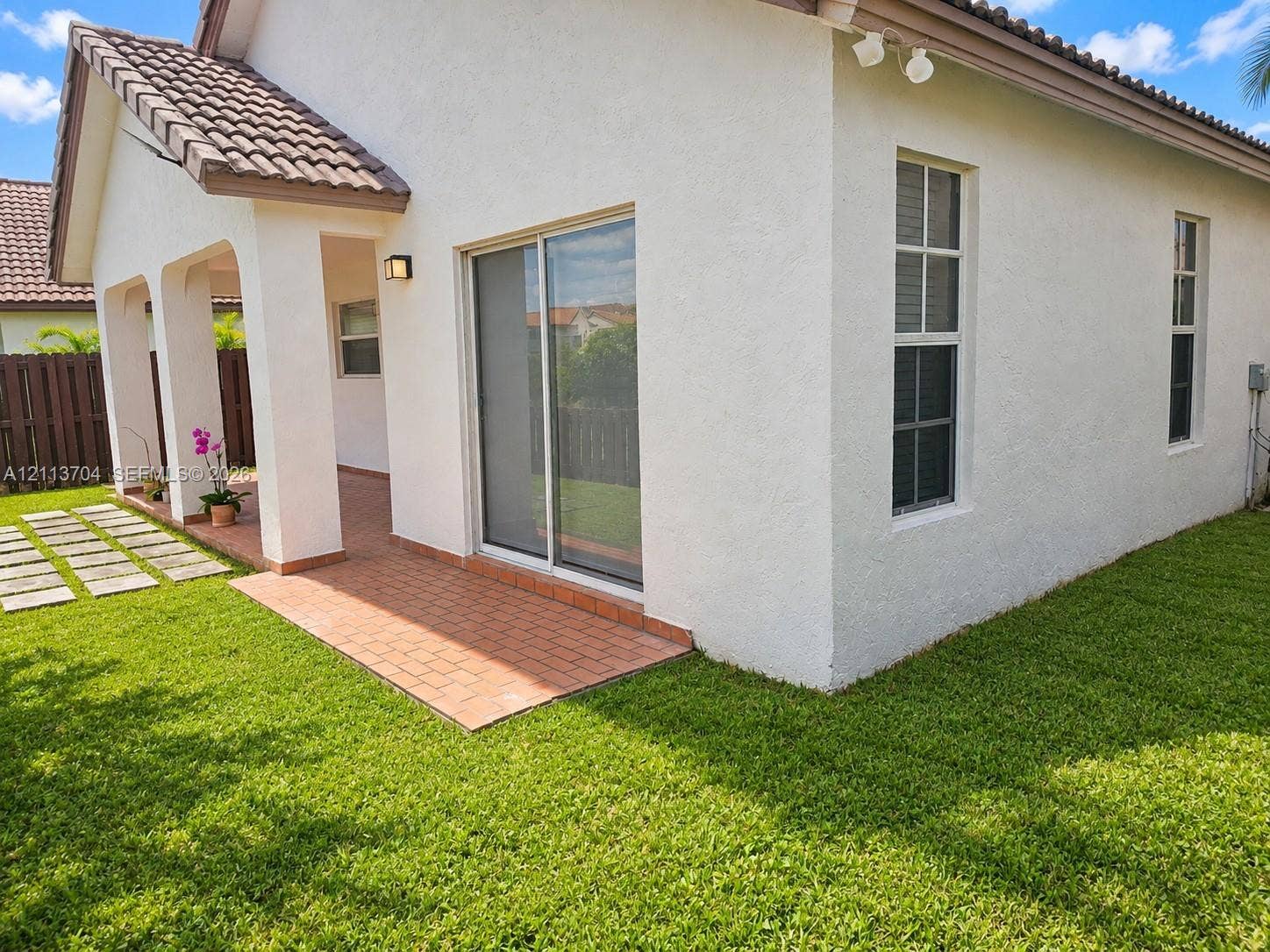 5254 SW 153rd Court, Miami, FL 33185 Stucco exterior featuring a covered patio, brick pavers, sliding glass doors, and a tiled roof