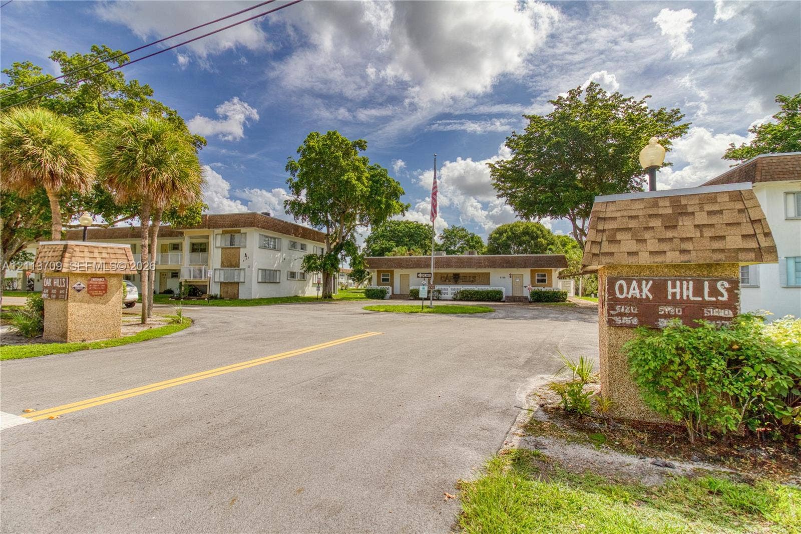 5170 SW 40th Avenue, #1E, Dania, Dania Beach, FL 33314 Multi-building property entrance featuring textured masonry signage, mature palm trees, asphalt paving, and established landscaping