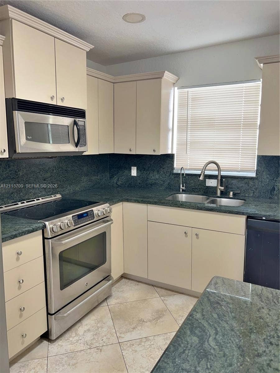 5170 SW 40th Avenue, #1E, Dania, Dania Beach, FL 33314 Kitchen featuring solid-surface countertops, custom shaker-style cabinetry, stainless steel appliances, a double-basin undermount sink with a gooseneck faucet, and tiled flooring