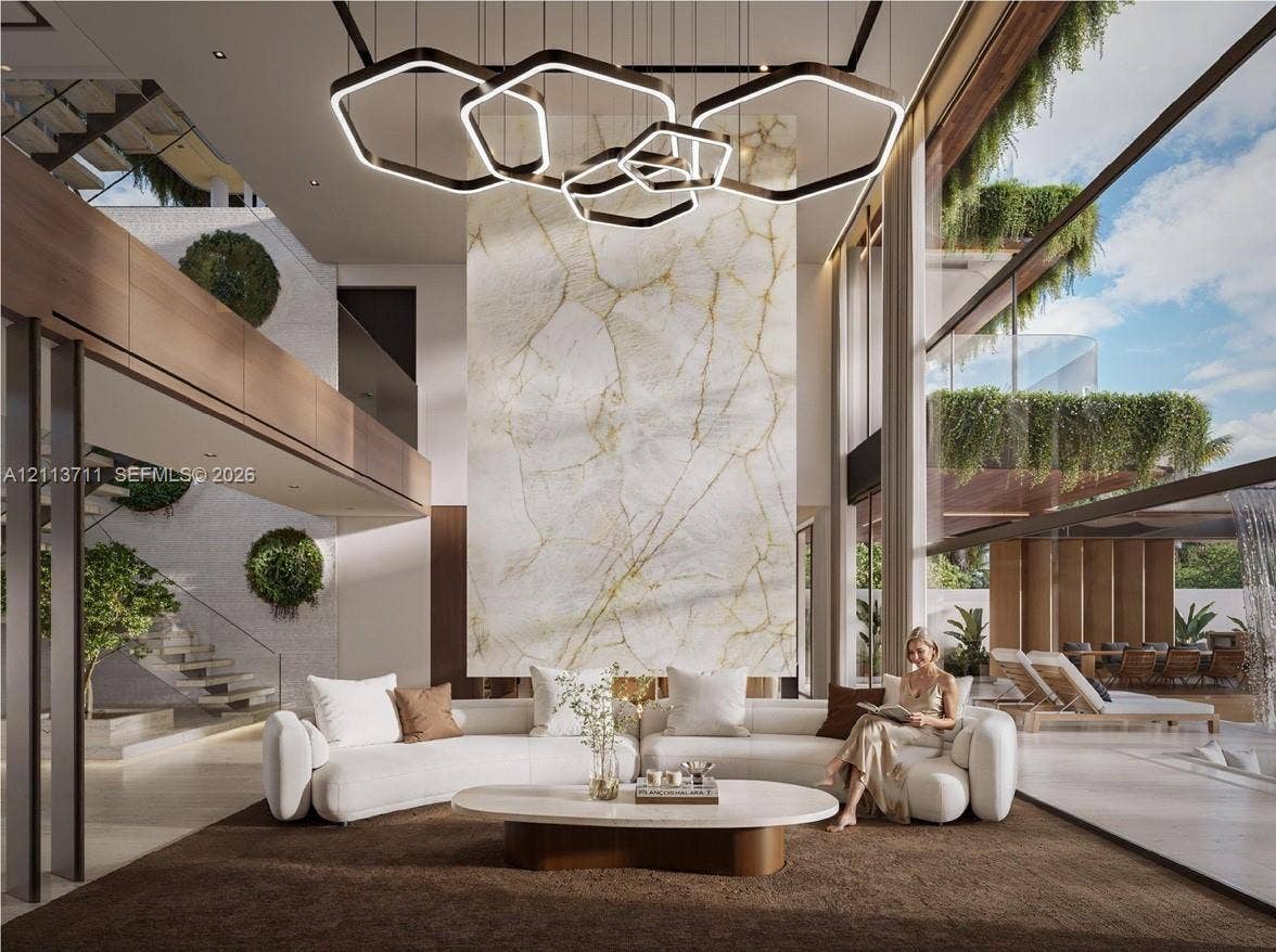 3322 NE 16th Court, Fort Lauderdale, FL 33305 Double-height ceiling, floor-to-ceiling glass walls, full-height stone-clad fireplace surround, custom geometric multi-tier pendant lighting, and floating staircase with glass railing