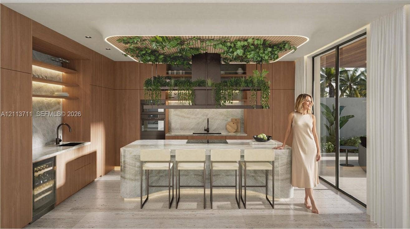 3322 NE 16th Court, Fort Lauderdale, FL 33305 Modern kitchen featuring full-height wood-finish cabinetry, a waterfall-edge stone island, built-in wine refrigeration, integrated ceiling lighting, and floor-to-ceiling glass sliding doors