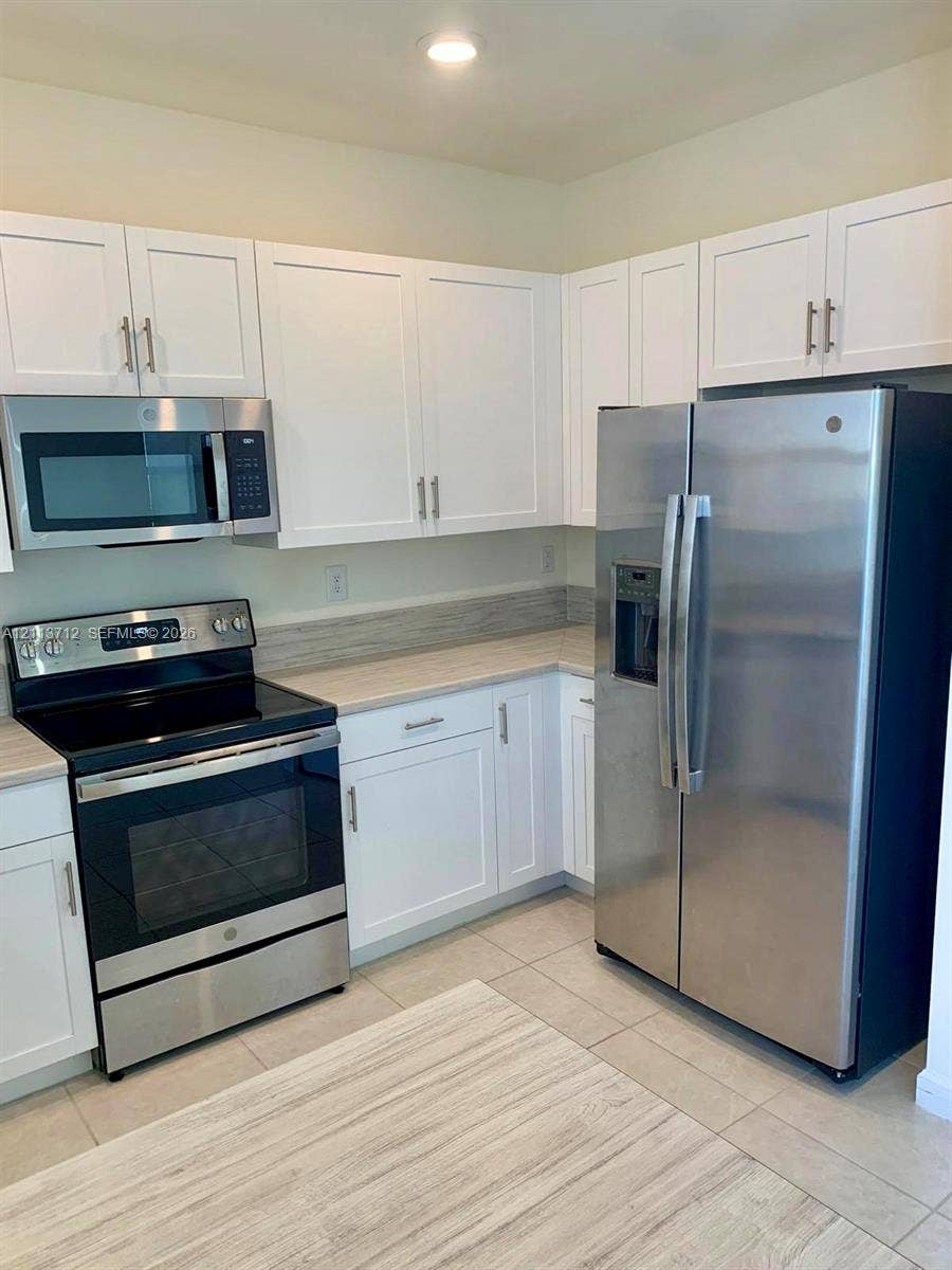10906 W 33rd Court, Hialeah, FL 33018 Kitchen featuring white shaker-style cabinetry, stainless steel appliances, neutral countertops, and tile flooring