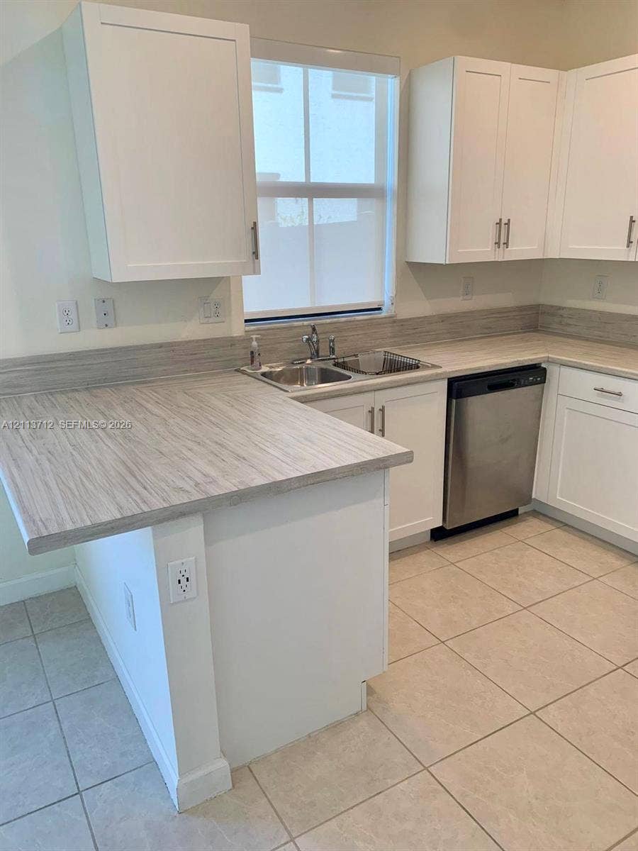 10906 W 33rd Court, Hialeah, FL 33018 Kitchen featuring white shaker-style cabinetry, neutral-toned countertops with matching backsplash, stainless steel dishwasher, dual-basin stainless steel sink, and light-colored tile flooring