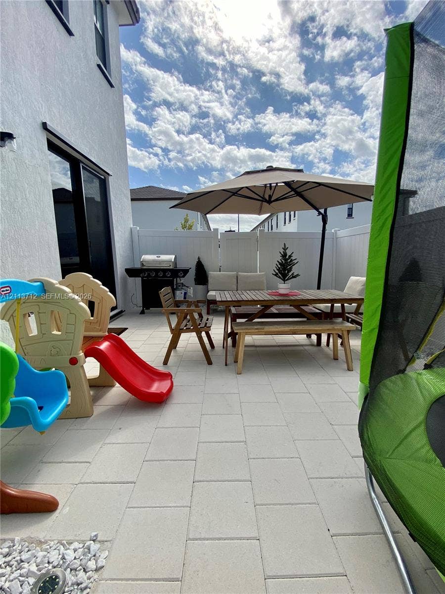 10906 W 33rd Court, Hialeah, FL 33018 Patio area featuring light-toned concrete pavers, full-height white vinyl perimeter fencing, and a smooth stucco exterior finish